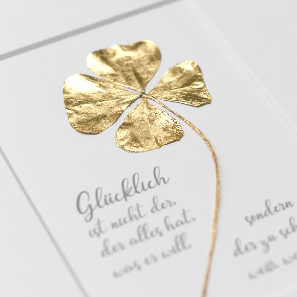 Echtes vierblättriges Kleeblatt mit Spruch, vergoldet mit 23,5 Karat Echtgold. Text: "Glücklich ist nicht der, der alles hat, was er will, sonder de der zu schätzen weiß, was er hat"